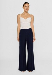 Bredbenede navy bukser med lodrette striber, featuring en høj talje og en blød tekstur. Sammen med en simpel hvid camisole top.