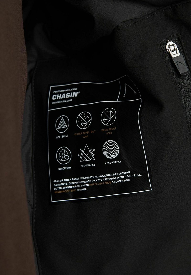 Czarna podszewka kurtki z białą metką z ikonami i tekstem opisującym jej właściwości odporności na wodę, wiatroszczelności i oddychalności.