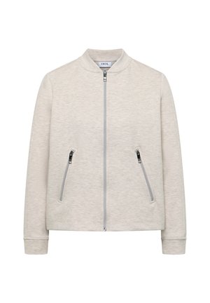 Světle béžová bunda na zip s dvěma nakloněnými kapsami na zip a malým stojáčkem, vyrobená z měkké texturované látky.