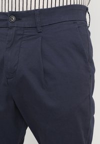 Granatowe bawełniane spodnie z zapięciem na guzik, plisami z przodu, bocznymi kieszeniami i gładką fakturą.