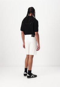 Black cropped knit sweater, white denim shorts with back pockets, black sneakers with white accents, standing in a neutral background.