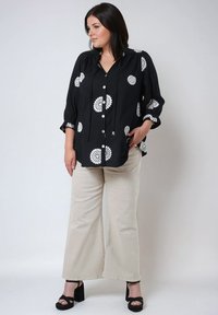 Black button-up shirt with white floral embroidery, long sleeves, rounded hem. Paired with beige wide-leg pants and black platform sandals.