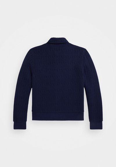 Tumši zila adīta jaka ar faktūrētu kabeļu rakstu, ar apkakli un ribotas piedurknes un apakšmalu, kas nodrošina pieguļošu siluetu.