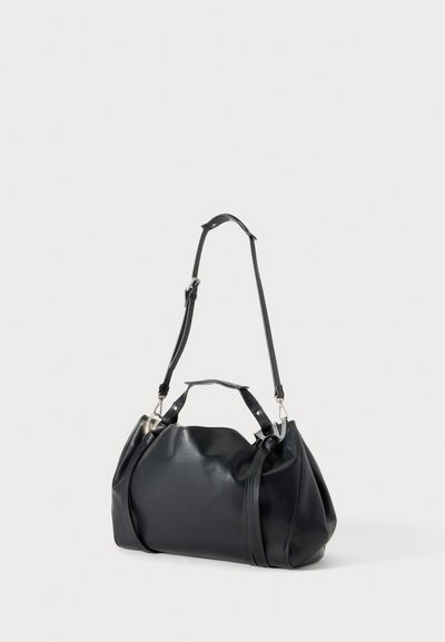Sac à main en cuir noir avec deux poignées et une longue bandoulière réglable, présenté debout sur un fond clair uni.