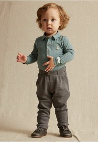 Vaaleanvihreä pitkähihainen paita, jossa on tähtikuvio ja karhun päällyspistoke, yhdistettynä harmaisiin housuihin. Ruskeat kengät täydentävät asu.