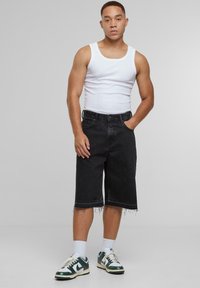 Svarte denimshorts med rå kanter, stylet med en hvit tanktopp. Fottøyet har et grønt, hvitt og svart sneakersdesign.