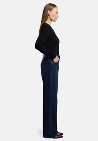 Jeans ampi di colore blu scuro con vita alta, texture liscia e tasche laterali, abbinati a un top nero a maniche lunghe.