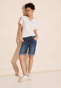 Vit kortärmad topp med texturerad tyg, kombinerad med knälånga blå denimshorts med uppvikta ben och fickor. Vita sneakers.