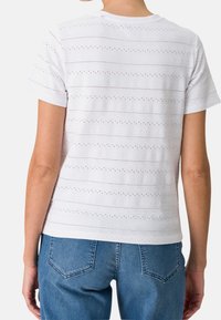 T-shirt blanc à manches courtes avec des motifs rayés horizontaux et des détails en œillets. Associé à un jean en denim bleu clair.