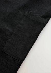 Tissu en coton noir avec une poche visible sur le côté. Texture lisse avec des variations subtiles de couleur, sans motifs ni détails matériels.