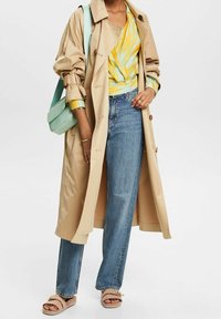 Trench beige, haut à motifs jaunes et bleus, jean bleu clair et sandales marron clair. Accessoires comprenant un sac bandoulière vert menthe.