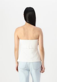 Biely top bez ramienok s priliehavým strihom, ktorý sa vyznačuje hladkou textúrou a lemom v štýle peplum, skombinovaný so svetlomodrými džínsy.