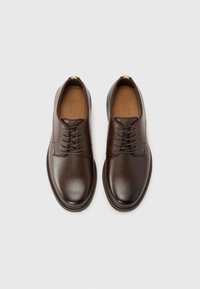 Chaussures habillées en cuir marron avec une finition lisse, un bout arrondi et un design à lacets à six œillets. Les semelles sont légèrement texturées pour une meilleure adhérence.