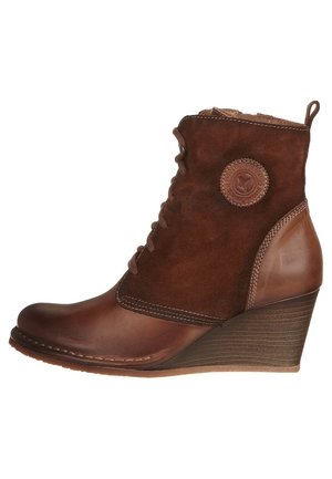 Bottine en cuir marron et suède avec un talon compensé, présentant un patch logo rond, un devant lacé et des coutures décoratives.