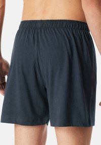 Pantaloni corti blu scuro in cotone con vita elasticizzata, caratterizzati da una texture liscia e un taglio dritto, visti da dietro.