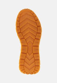 Suola in gomma per sneaker con un motivo a zigzag arancione. Nome del marchio "GUESS" impresso al centro. Testurizzata per grip e supporto.