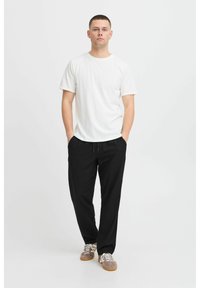 White cotton t-shirt, black relaxed trousers, and gray sneakers with white laces. Model standing with hands in pockets on a plain background.