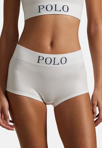 Zbliżenie osoby noszącej białą prążkowaną bieliznę i dopasowany sportowy biustonosz z napisem "POLO" na elastycznych paskach w talii.