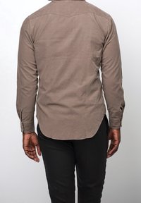 Bruine longsleeve met een inzetstuk en een afgeronde zoom, gemaakt van zacht stof, gecombineerd met een donkere broek. Zichtbare manchetten met knopen.