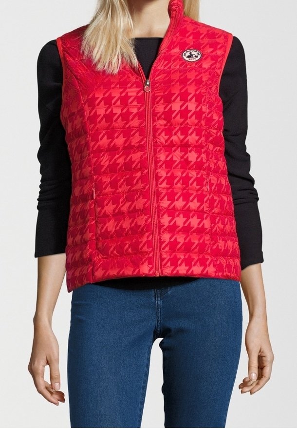 Czerwony pikowany kamizelka z wzorem w piedzie, z zapięciem na zamek błyskawiczny z przodu i logo po lewej stronie klatki piersiowej. Nosi się na czarnej koszuli z długim rękawem.