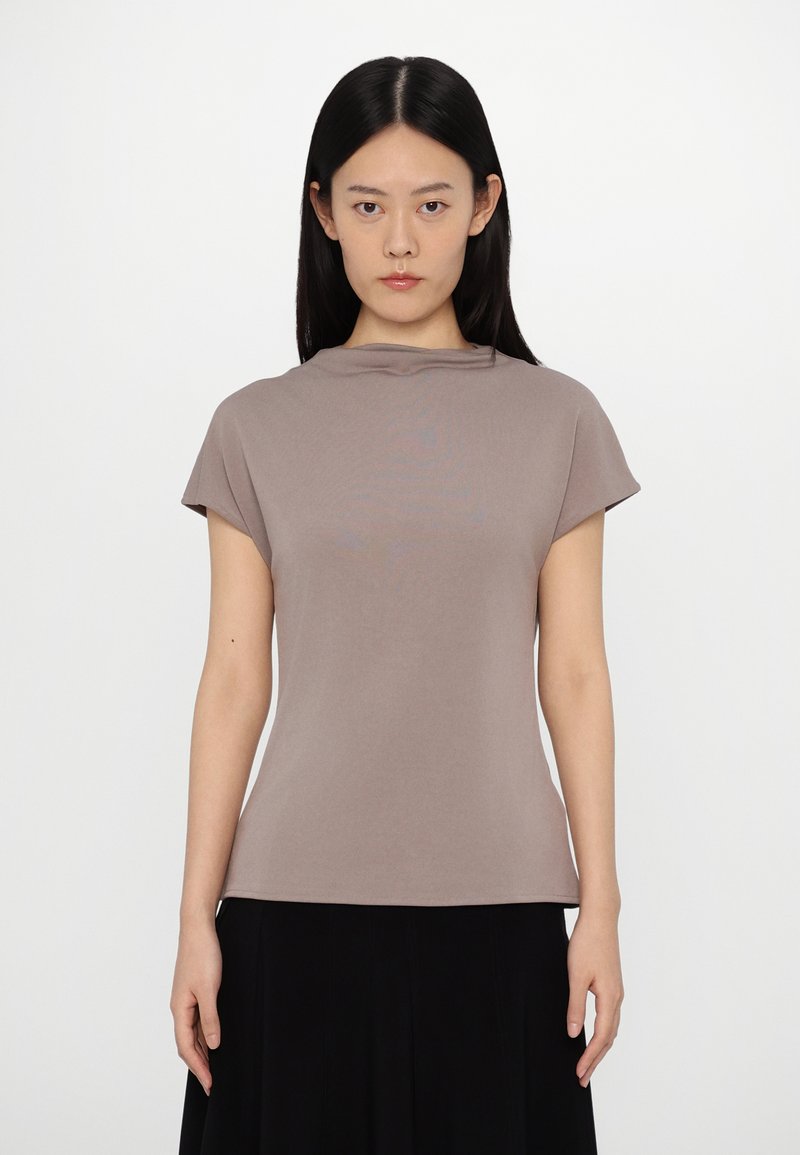 Top marrone a maniche corte realizzato in tessuto liscio, con un collo rilassato e una silhouette slim e aderente. Indossato con una gonna nera.