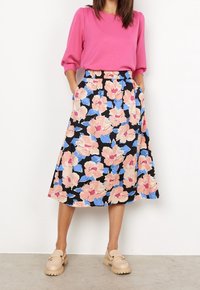 Rosa Langarmshirt mit einem schwarzen Midirock mit großen pinken und blauen Blumen, Seitentaschen und entspannter Passform. Beige klobige Loafers.