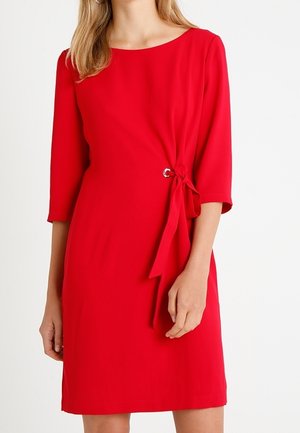 Czerwona sukienka do kolan z rękawami o długości do połowy przedramienia, z bocznym wiązaniem i okrągłym akcentem. Gładka tkanina z dopasowanym krojem.