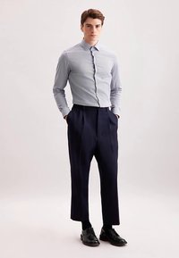 Lichtblauw gestreept overhemd met knopen, op maat gemaakte marineblauwe broek en zwarte oxford schoenen. De outfit heeft een aansluitend ontwerp en een gladde textuur.