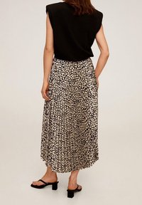 Top nero senza maniche con spalline abbinato a una gonna plissettata maxi con motivo crema e nero. Modella che indossa sandali neri con tacco blocco.
