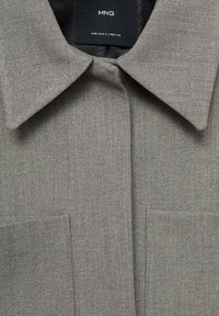Camicia grigia con colletto in tessuto testurizzato, dotata di patta frontale e due tasche sul petto, che presenta un design classico.