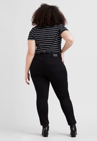 Černé skinny džíny a černo-bílý pruhovaný krátký rukáv, zobrazené zezadu, s štítkem na pásku a texturovanou látkou.