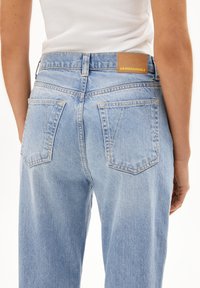 Jeans in denim azzurro chiaro con vita alta, design a gamba dritta, tasche posteriori e un'etichetta marrone con la scritta "ARMEDANGELS" sulla vita.