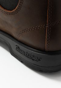 Hněd�á kožená bota s černou gumovou podrážkou, se zřetelným švem a logem vyraženým na boku. Hladký povrch a robustní design.