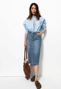 Chemise surdimensionnée bleu clair à boutons, jupe crayon en denim taille haute, sac à franges marron et chaussures noires à enfiler.