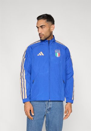 Veste légère bleue avec des bandes dorées le long des manches, un logo "Italia" sur la poitrine et des poches latérales zippées.