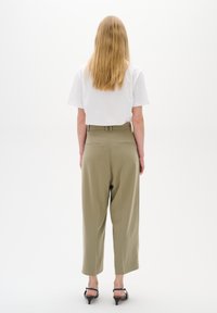 Kakifärgade skräddarsydda byxor med hög midja, vida ben och bakfickor, i kombination med en enkel vit t-shirt med kort ärm. Svarta klacksandaler.