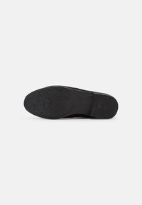 Suela de zapato negra con superficie texturizada que presenta patrones florales. Tiene bordes suaves y una ligera curvatura, además de un acabado mate.