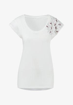 Camiseta de algodón blanca con mangas cortas, que presenta flores rojas bordadas y hojas verdes en el hombro izquierdo. Cuello redondo.