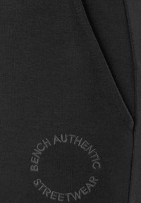 Schwarze Jogginghosen aus weichem Stoff, mit einer Seitenasche und geprägtem Logo "BENCH AUTHENTIC STREETWEAR" im kreisförmigen Design.