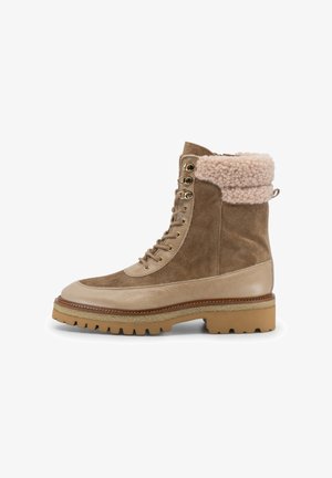 Botas de ante marrón con un puño de pelaje sintético crema. Presentan una puntera redondeada, suela texturizada y ojales metálicos para los cordones.