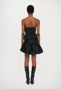 Black dress with a fitted smocked bodice and layered ruffle skirt, featuring thin straps and a textured finish. Knee-high black boots.