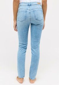 Světle modré džíny s vysokým pasem, slim fit, pěti kapsami a minimem švů, zobrazené zezadu.