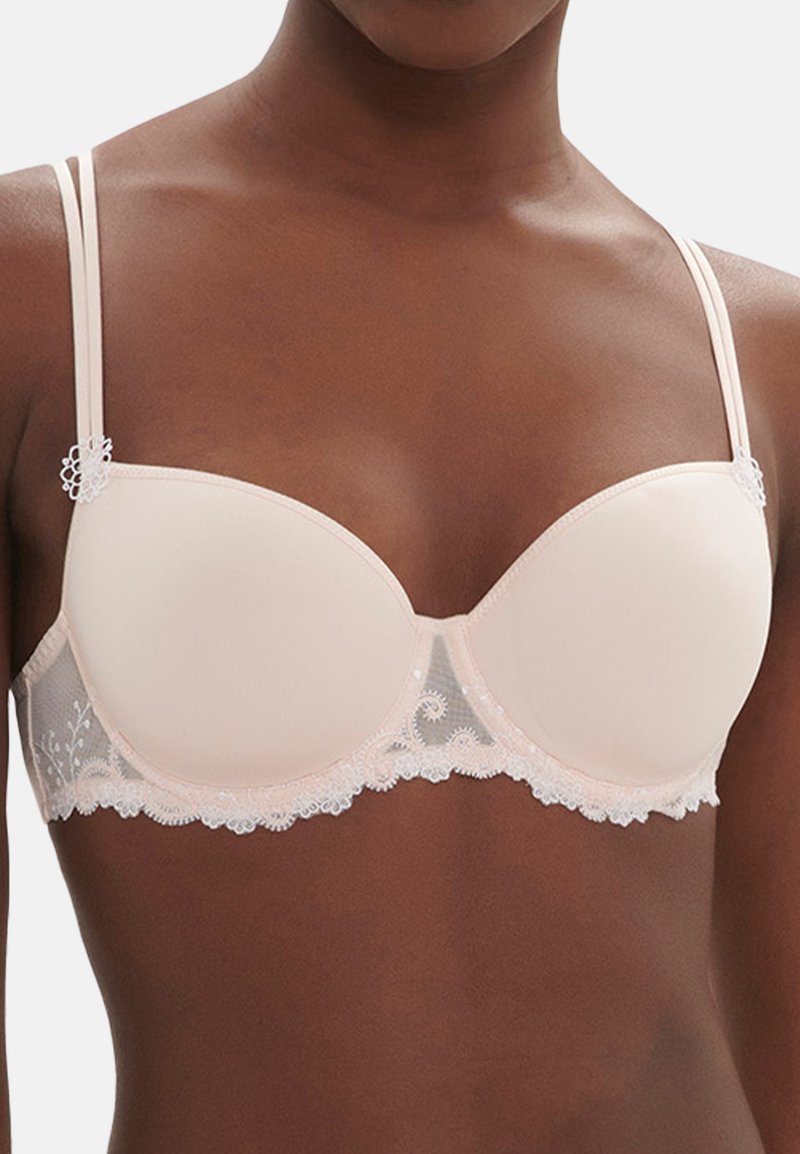 Ondersteunende bh met een gladde nude cup, een delicate kantdetail bij de band, verstelbare bandjes en bloemaccenten dicht bij de randen.