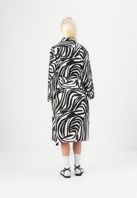 Rochie lungă cu dungi de zebra alb-negru, cu talie legată, având mâneci lungi și o croială relaxată. Purtată cu șosete albe și sandale.