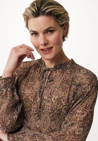 Brun paisley-bluse med blød tekstur, flæset halsudskæring og lange ærmer, prydet med indviklede blomster mønstre i orange, grøn og sort.