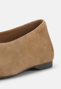 Suede-braune flache Schuhe mit abgerundeter Spitze und niedrigem schwarzen Absatz. Sie besitzen ein schlankes Design mit glatter Textur und minimaler Detailgestaltung.