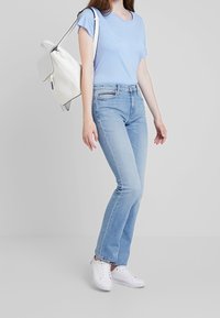 Camiseta de manga corta azul claro, jeans rectos azul claro y zapatillas blancas. Un bolso blanco con detalles negros se lleva sobre el hombro.