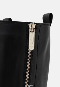 Czarny skórzany but o gładkiej fakturze, z złotym zamkiem błyskawicznym, oznaczeniem marki oraz dwoma górnymi uchwytami.