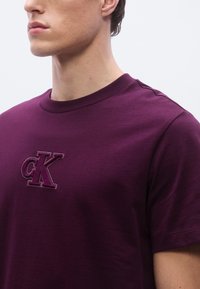 Maroon cotton t-shirt featuring a crew neck and embroidered cK logo in a darker shade. Smooth texture with short sleeves.