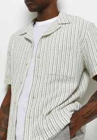 Lyhythihainen nappipaita, jossa on vaaleanruskeat ja mustat raidat, yksittäinen rintatasku ja pehmeä, teksturoitu kangas.